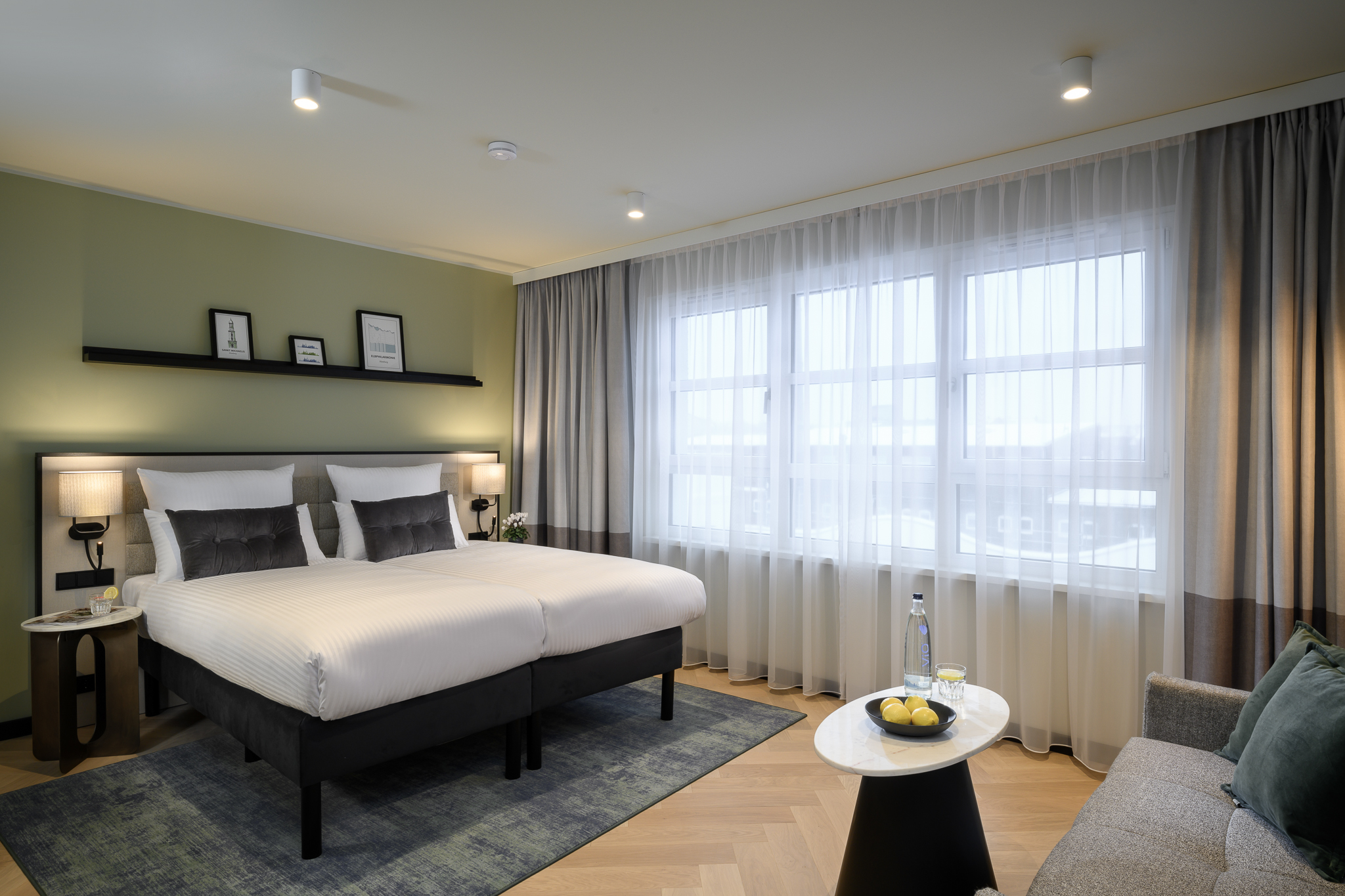 A compact studio with a gray sofa, small table, and window with sheer curtains