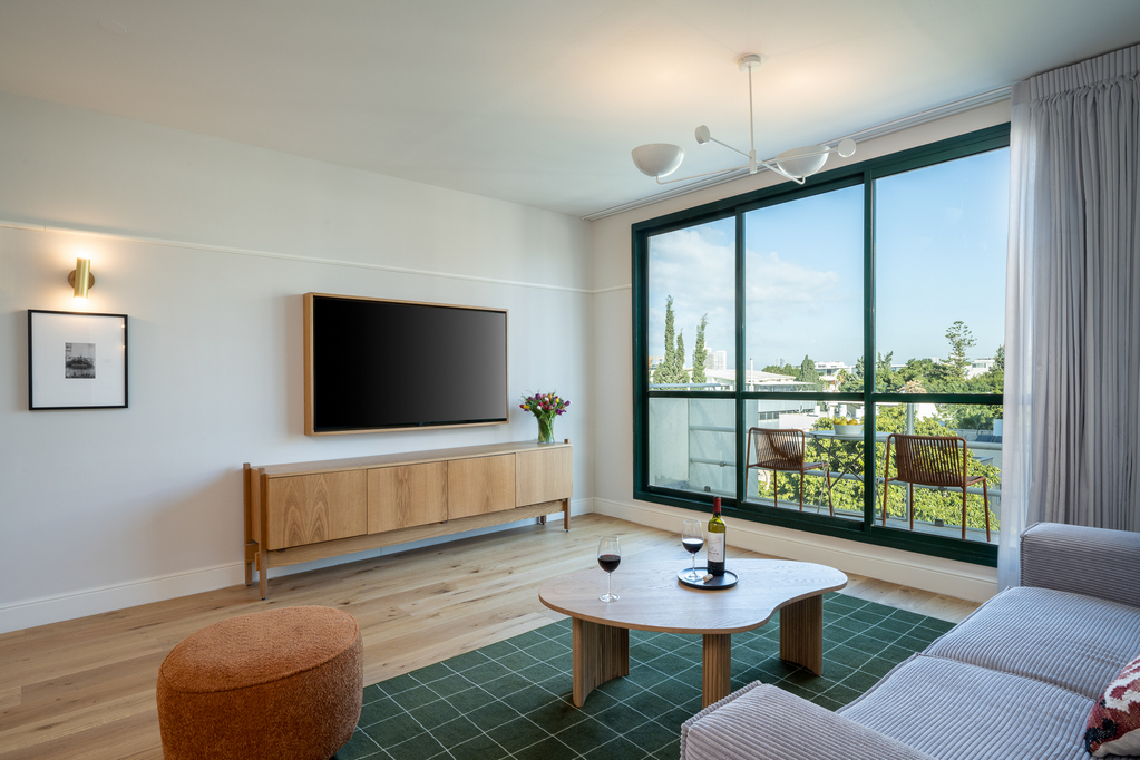 Modern living space in the One-Bedroom with Balcony at master Mazeh Tel Aviv, with floor-to-ceiling glass doors connecting to the outdoor balcony.