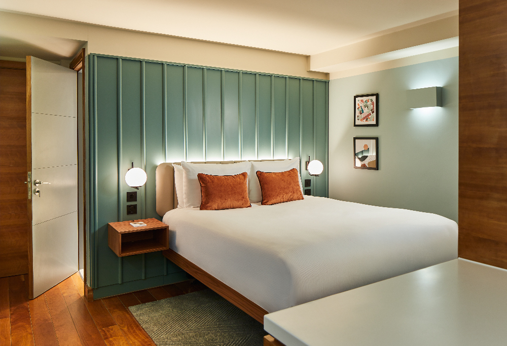 Cozy bedroom at master Farringdon London serviced apartments, featuring a modern bed with orange pillows, soft lighting, and green panel headboard.