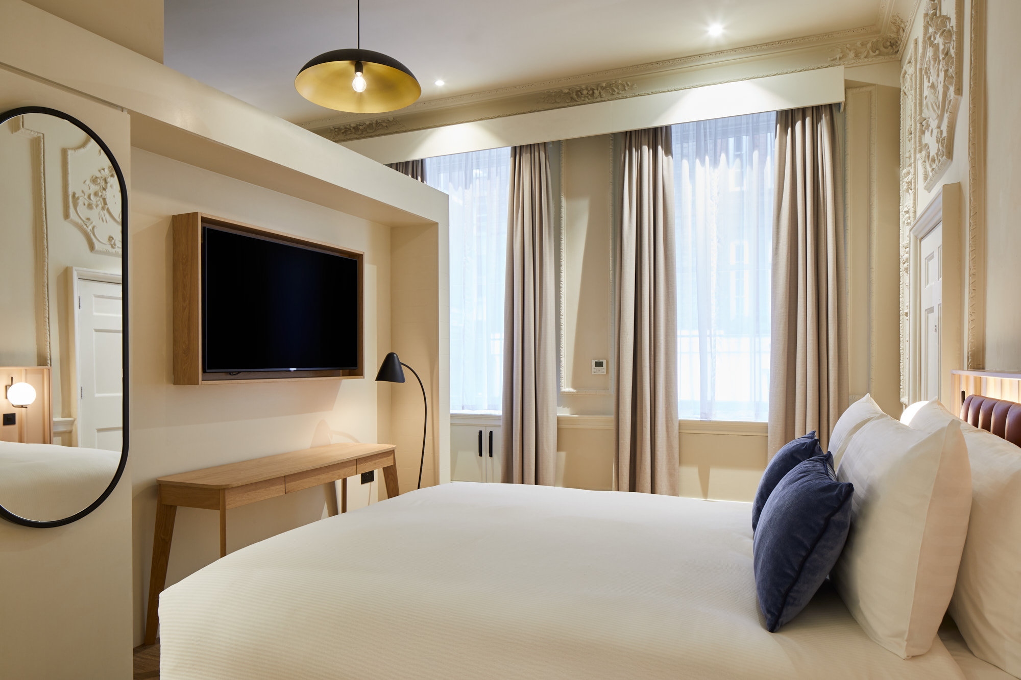 Bedroom with large bed, two blue pillows, and tall windows framed by elegant curtains and decorative wall detailing.