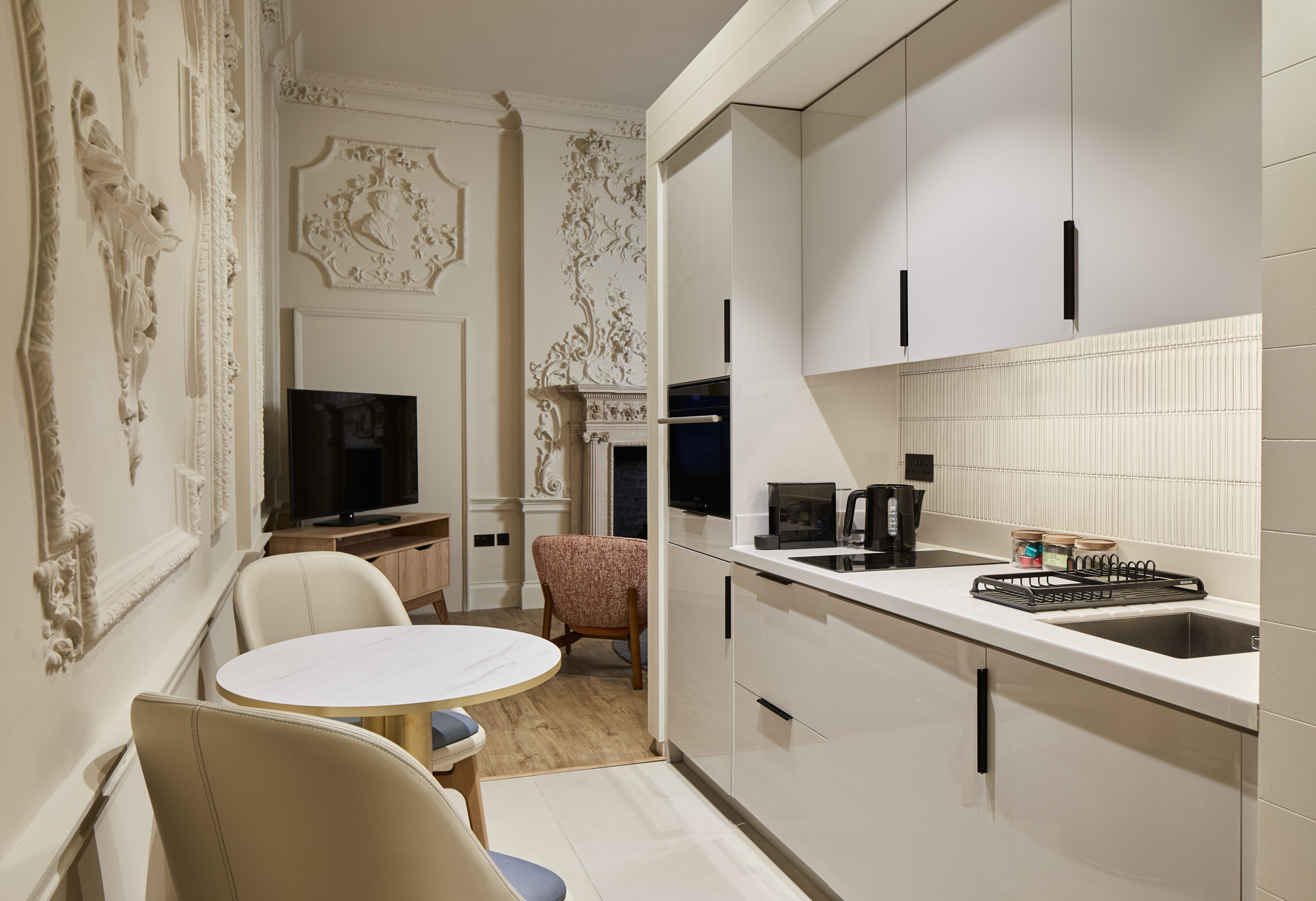 Kitchenette and dining area with modern white cabinetry and ornate historic wall decorations.