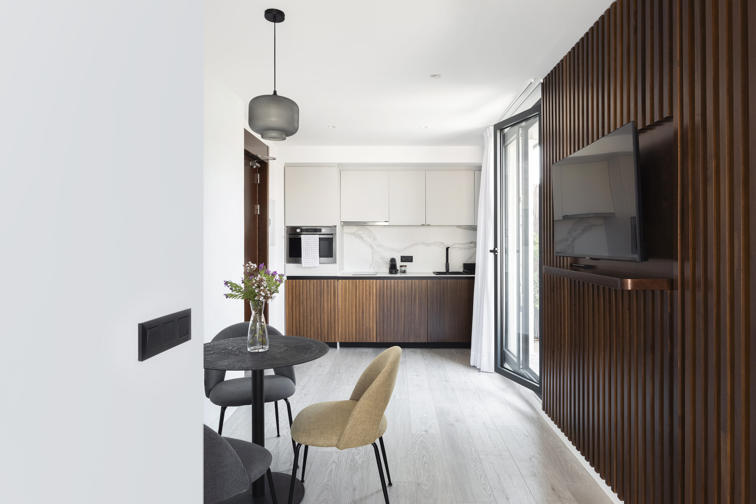 Modern open-plan kitchen and dining space at master La Rambla Barcelona featuring wood finishes, marble backsplash, and flat-screen TV.