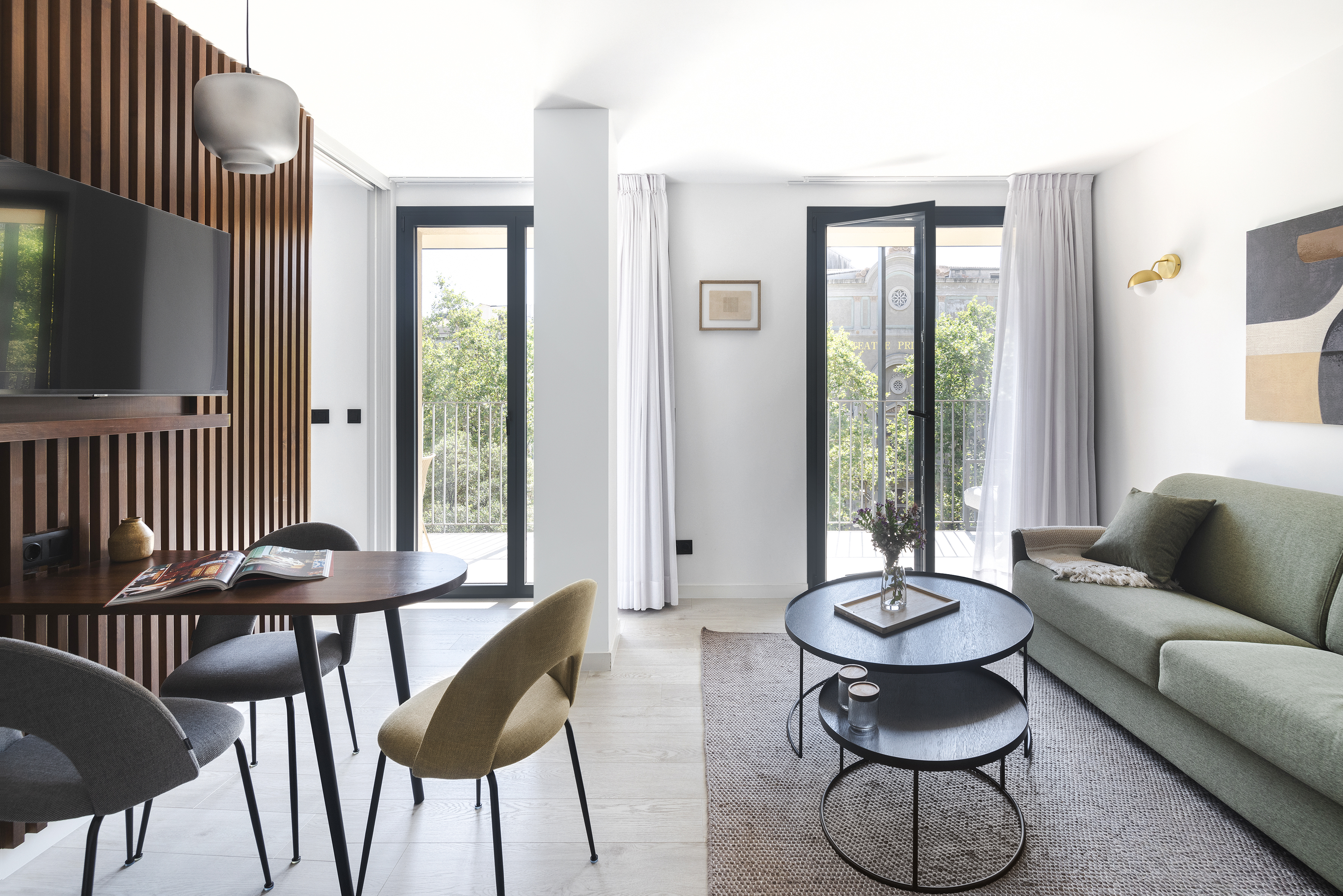 Modern living room at master La Rambla Barcelona with green sofa, dining table, and balcony doors bringing in natural light.