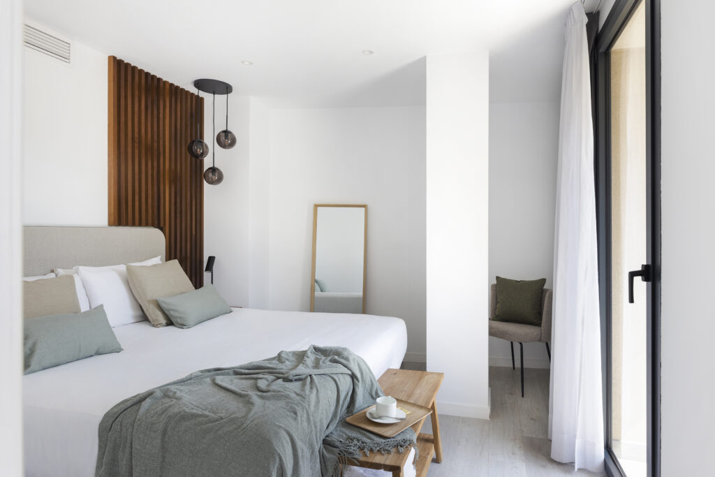 Bright bedroom at master La Rambla Barcelona with double bed, wood-panel accent wall, pendant lights, and full-length mirror.