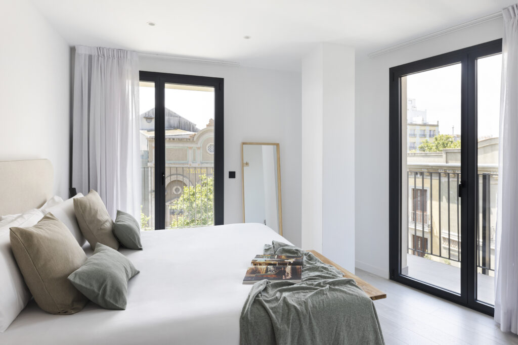Spacious bedroom at master La Rambla Barcelona with double bed, soft neutral décor, large windows, and views of Barcelona’s architecture.