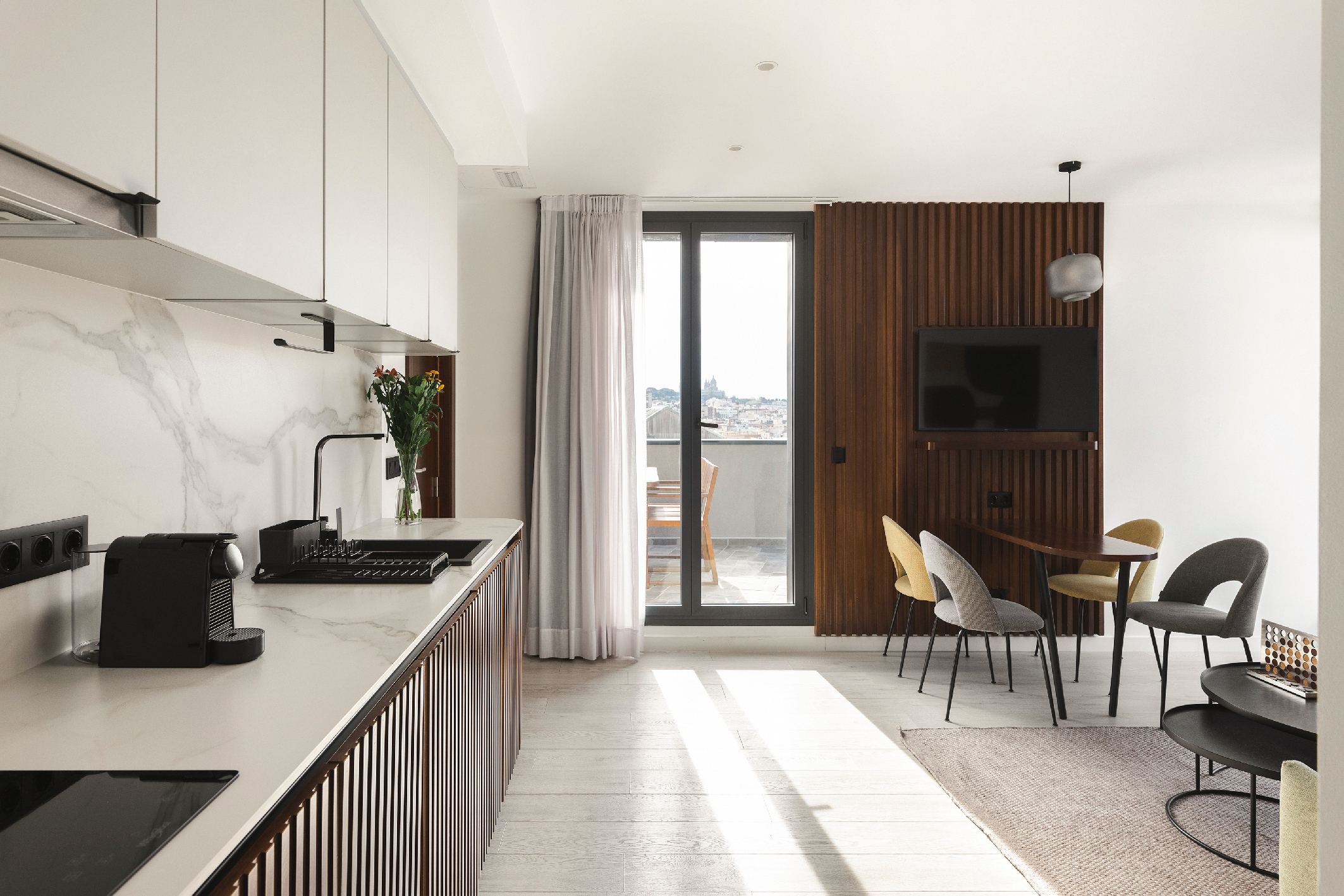 Modern penthouse kitchen with marble backsplash, sleek cabinets, and dining area facing terrace with views of Barcelona.