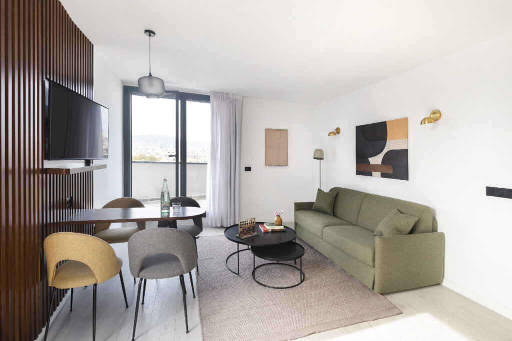 Contemporary penthouse living room with green sofa, wood accents, and full kitchen, opening onto a private terrace.