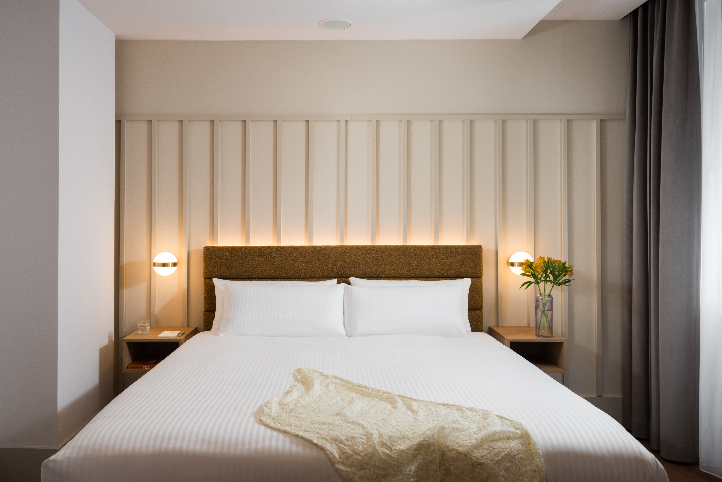 Minimalist bedroom at master Wola Serviced Apartments featuring a double bed, padded headboard, and warm bedside lighting