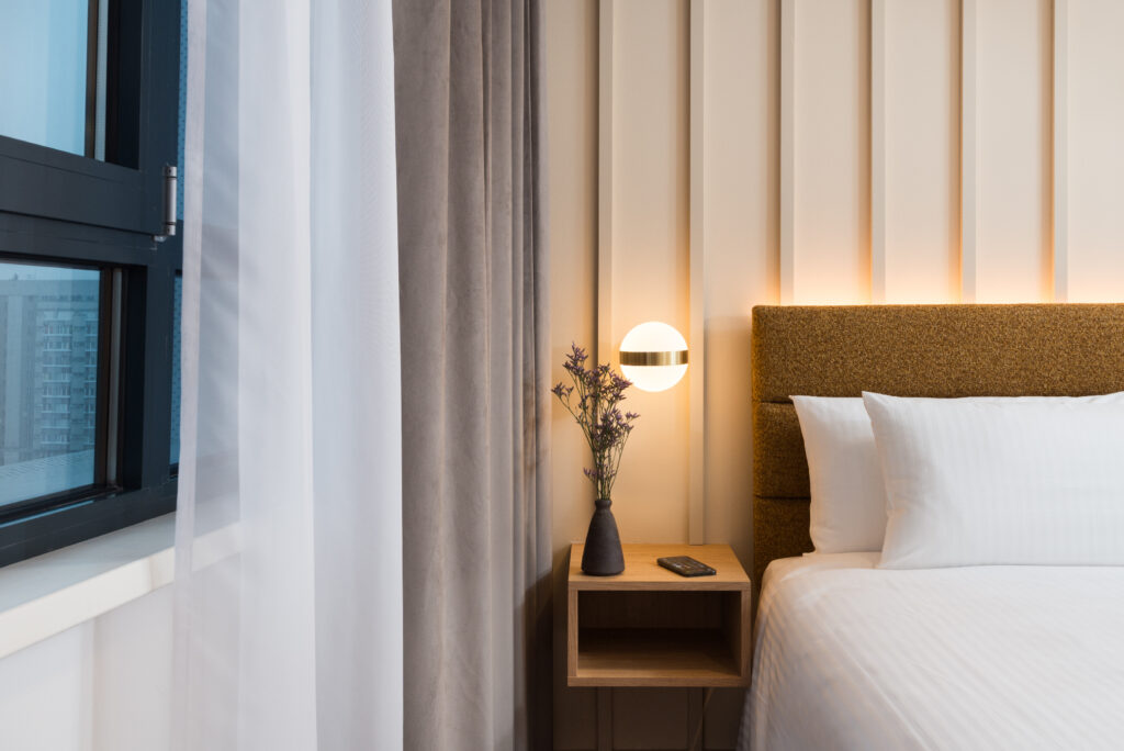 Bedside detail in a studio apartment at master Wola Serviced Apartments with warm lighting, curtains, and nightstand