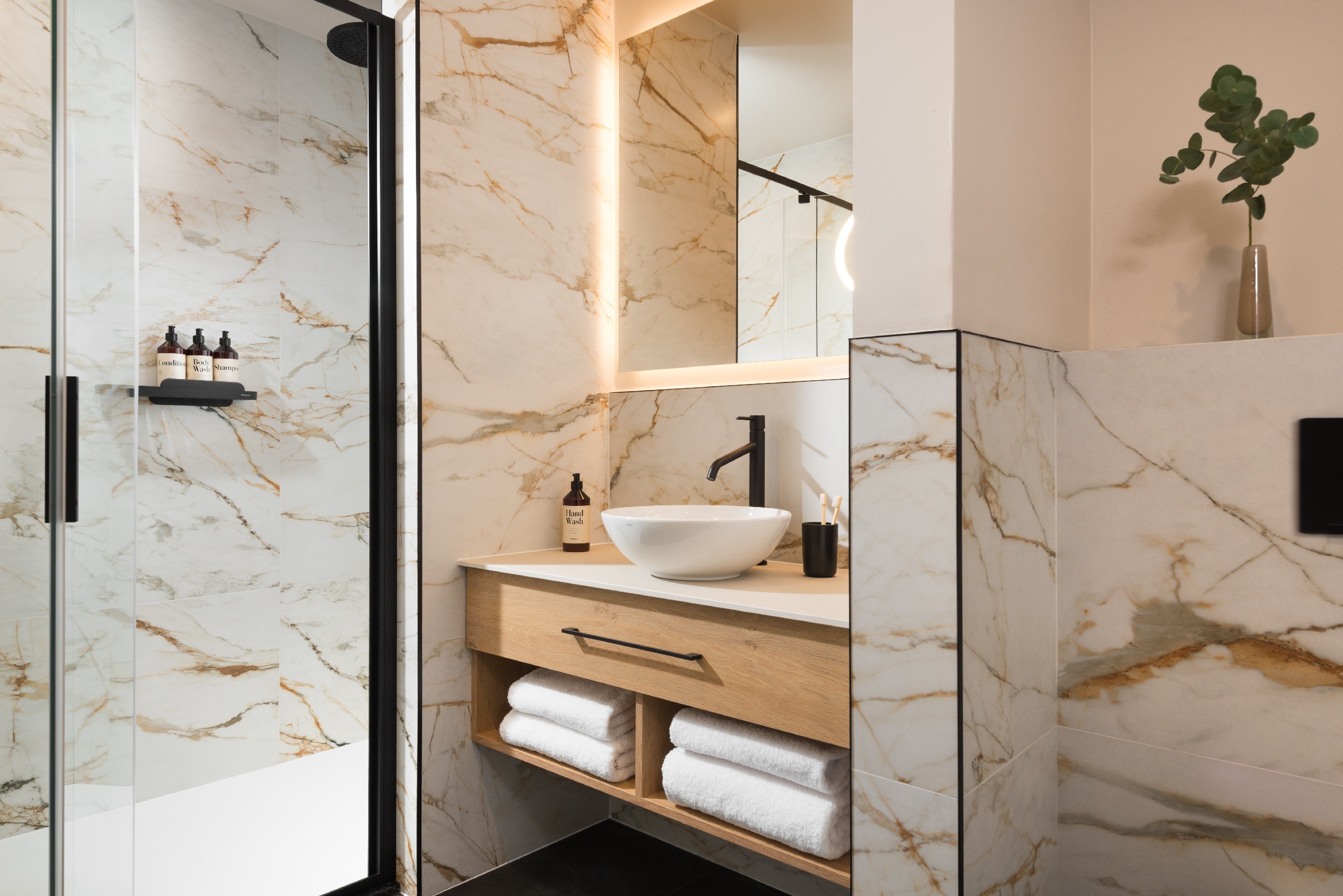 Modern bathroom at master Wola Serviced Apartments with walk-in shower, marble-style tiles, and vanity unit