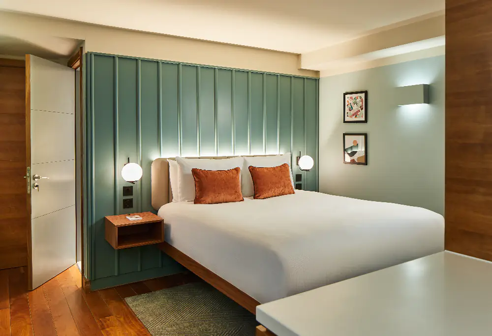 Cozy bedroom at master Farringdon London serviced apartments, featuring a modern bed with orange pillows, soft lighting, and green panel headboard.