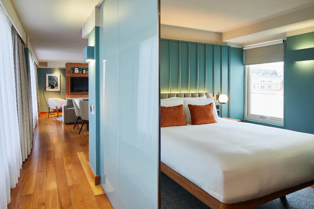 Contemporary bedroom space at master Farringdon London serviced apartments, separated by a glass wall, with a stylish bed, soft lighting, and city views through the window.