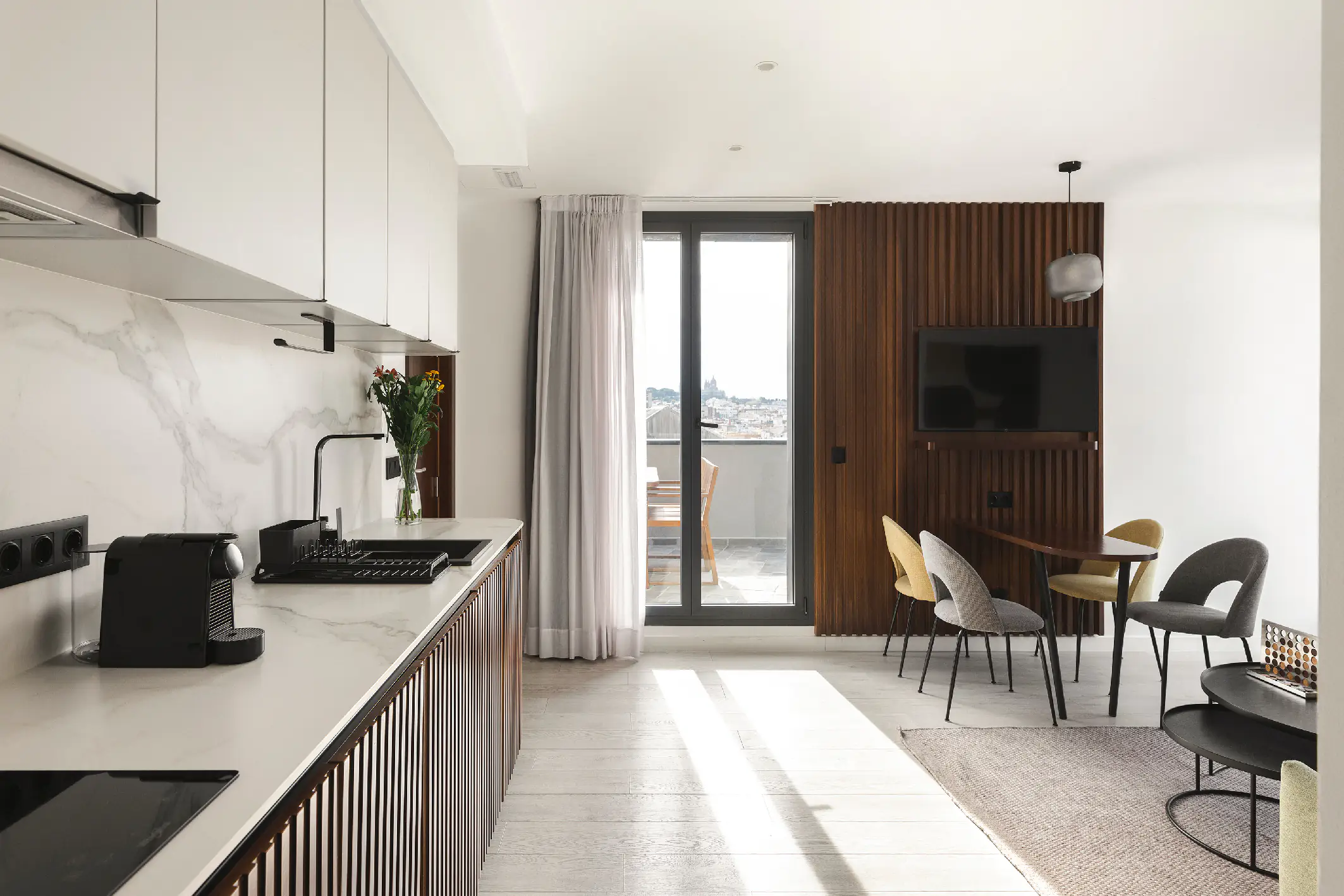 Modern penthouse kitchen with marble backsplash, sleek cabinets, and dining area facing terrace with views of Barcelona.
