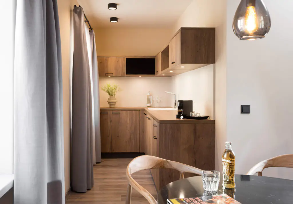 Modern kitchenette at master Linzergasse featuring wooden cabinets, ample counter space, espresso machine, and large windows with elegant curtains.
